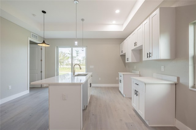 kitchen featuring white cabinetry, sink, an island with sink, and hanging light fixtures