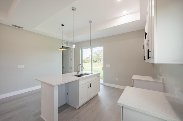 kitchen featuring a kitchen island with sink, sink, white cabinets, and light wood-type flooring