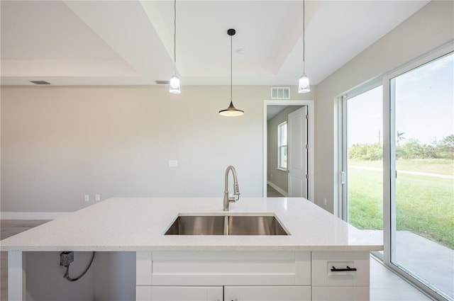 kitchen featuring light stone countertops, white cabinetry, sink, and pendant lighting