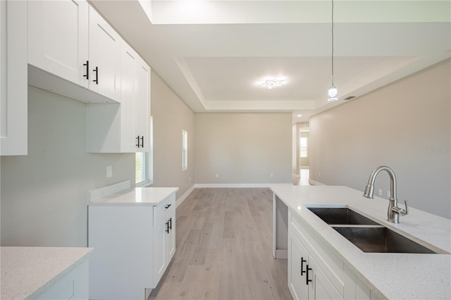 kitchen with pendant lighting, light wood-type flooring, a tray ceiling, and sink