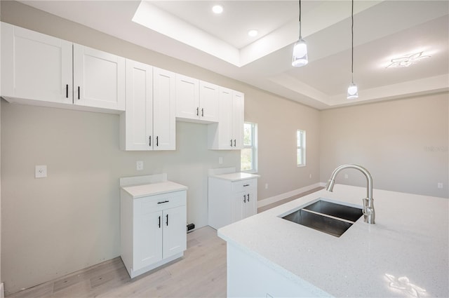 kitchen featuring a tray ceiling, sink, decorative light fixtures, light hardwood / wood-style flooring, and white cabinets