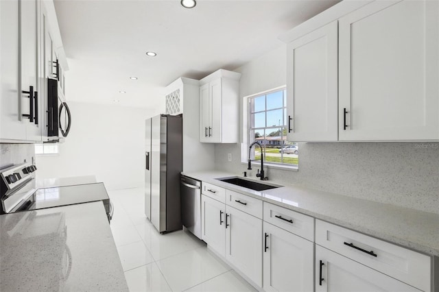 kitchen with light stone countertops, decorative backsplash, stainless steel appliances, sink, and white cabinetry