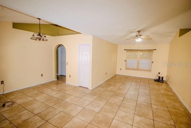 empty room with vaulted ceiling, light tile patterned floors, and ceiling fan with notable chandelier