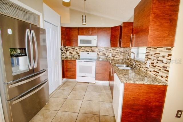 kitchen featuring backsplash, white appliances, vaulted ceiling, sink, and light tile patterned flooring