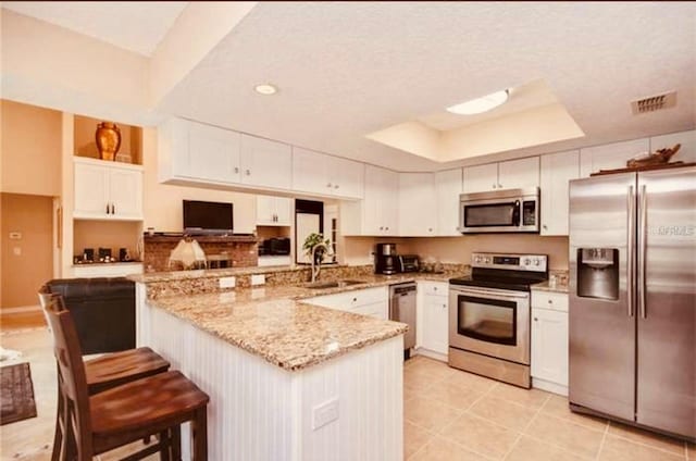 kitchen featuring a tray ceiling, kitchen peninsula, stainless steel appliances, light stone countertops, and white cabinets