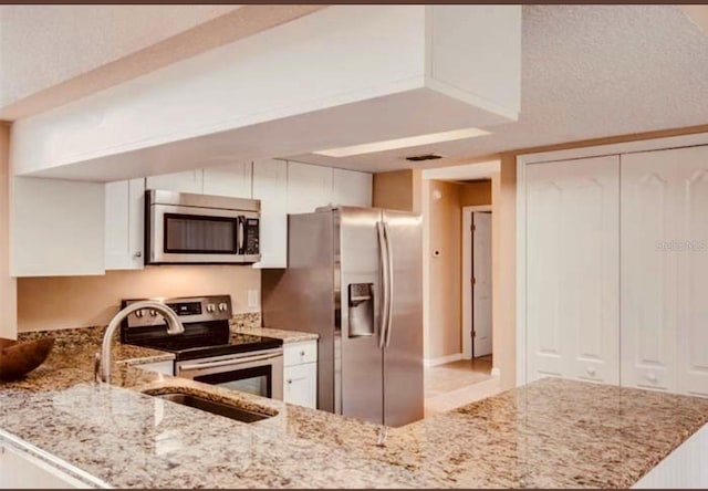 kitchen with stainless steel appliances, white cabinetry, light stone countertops, and kitchen peninsula