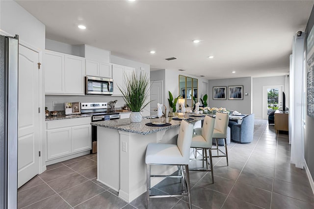 kitchen with white cabinets, a kitchen breakfast bar, an island with sink, light stone counters, and stainless steel appliances