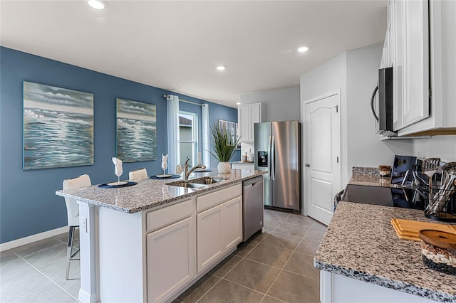 kitchen with light stone countertops, sink, stainless steel appliances, an island with sink, and white cabinets