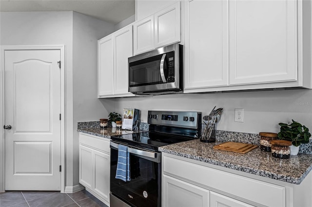 kitchen featuring white cabinets, appliances with stainless steel finishes, dark tile patterned floors, and dark stone counters