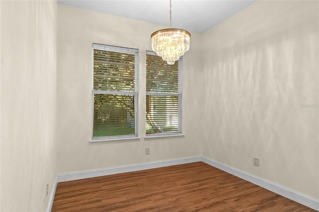 empty room featuring a notable chandelier and wood-type flooring