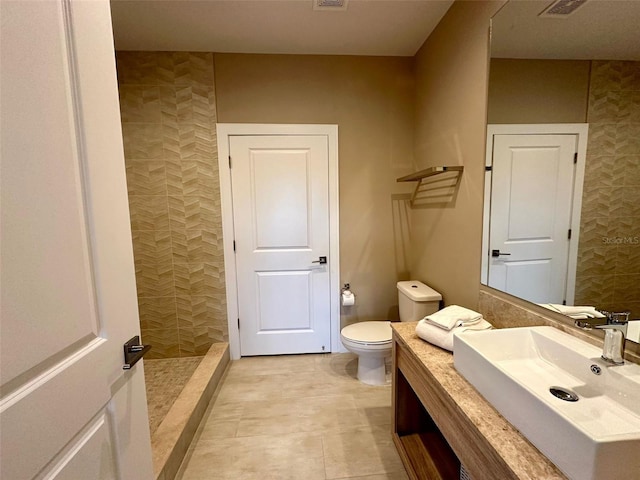 bathroom with tile patterned flooring, vanity, toilet, and a tile shower