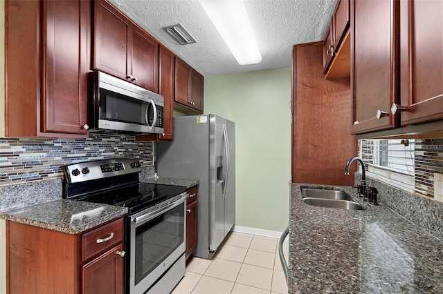 kitchen with dark stone counters, sink, light tile patterned floors, a textured ceiling, and stainless steel appliances