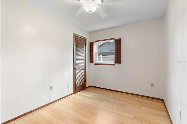 spare room with a textured ceiling, light hardwood / wood-style flooring, ceiling fan, and wood walls