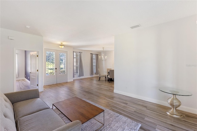 living room with light hardwood / wood-style flooring, french doors, and an inviting chandelier