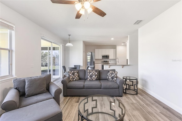 living room with ceiling fan, light wood-type flooring, and sink