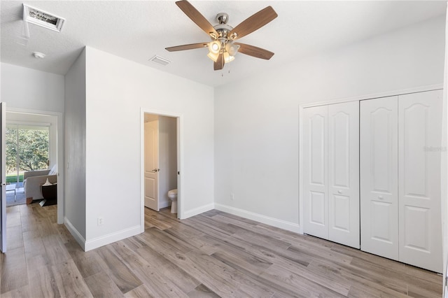 unfurnished bedroom with light wood-type flooring, a textured ceiling, ceiling fan, connected bathroom, and a closet