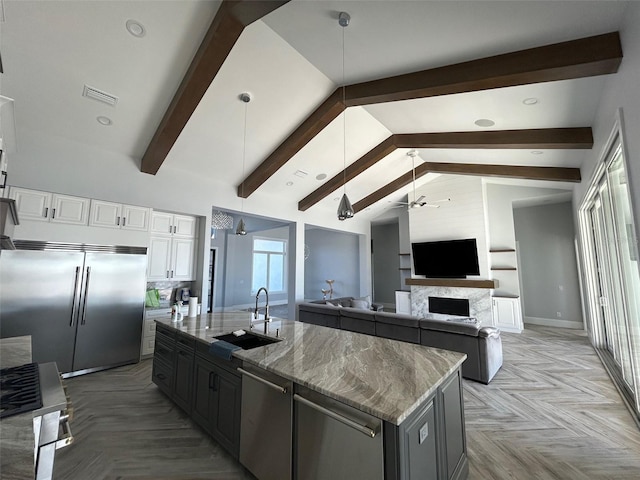 kitchen featuring white cabinetry, sink, vaulted ceiling with beams, an island with sink, and appliances with stainless steel finishes