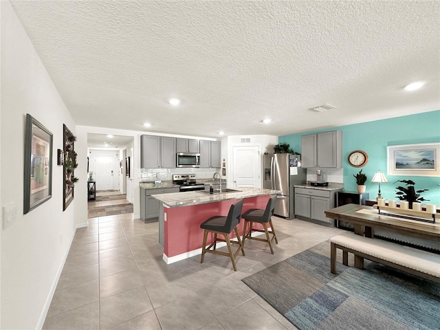 kitchen with appliances with stainless steel finishes, a kitchen island with sink, a kitchen breakfast bar, and gray cabinetry