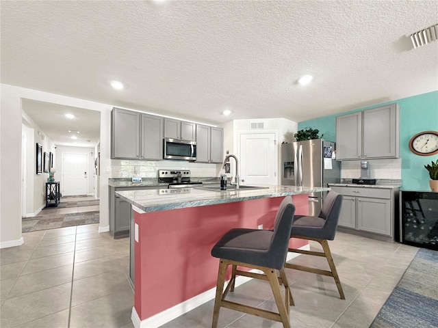 kitchen with gray cabinetry, a center island with sink, a breakfast bar area, decorative backsplash, and stainless steel appliances