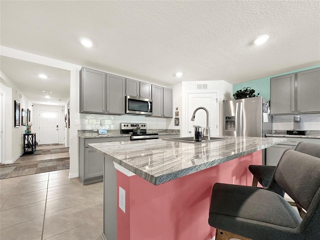 kitchen with sink, backsplash, an island with sink, a breakfast bar, and appliances with stainless steel finishes