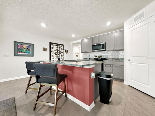 kitchen with gray cabinetry, tasteful backsplash, an island with sink, a breakfast bar, and appliances with stainless steel finishes