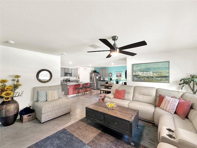 living room with ceiling fan, light tile patterned floors, and a textured ceiling