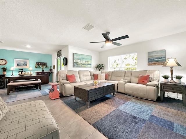 living room with a textured ceiling, ceiling fan, and light tile patterned flooring