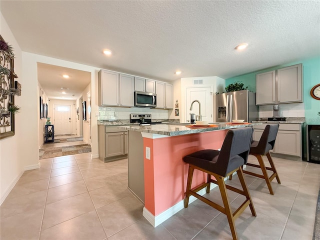 7729 Rosewood Garden Loop, Tampa, FL 33637 - kitchen with stainless steel appliances, gray cabinets, a breakfast bar area, an island with sink, and recessed lighting