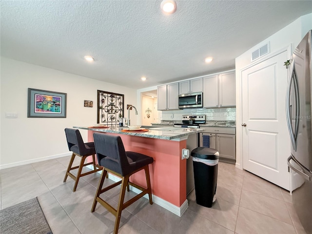 7729 Rosewood Garden Loop, Tampa, FL 33637 - kitchen featuring stainless steel appliances, a kitchen breakfast bar, gray cabinetry, a center island with sink, and recessed lighting