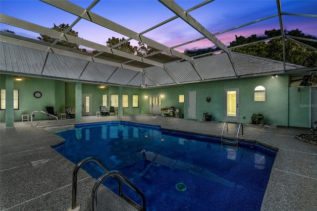 pool at dusk with glass enclosure and a patio