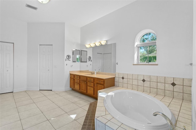 bathroom featuring tile patterned flooring, vanity, and tiled bath