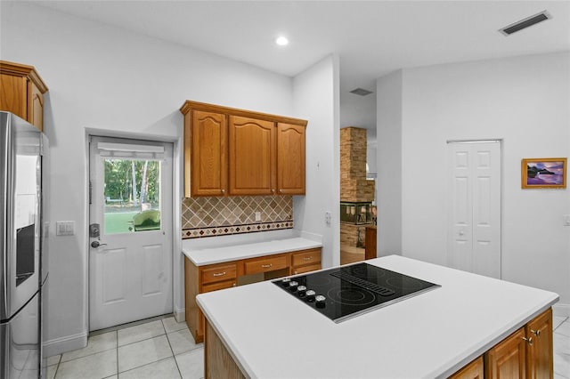 kitchen with tasteful backsplash, black electric cooktop, light tile patterned floors, a center island, and stainless steel refrigerator