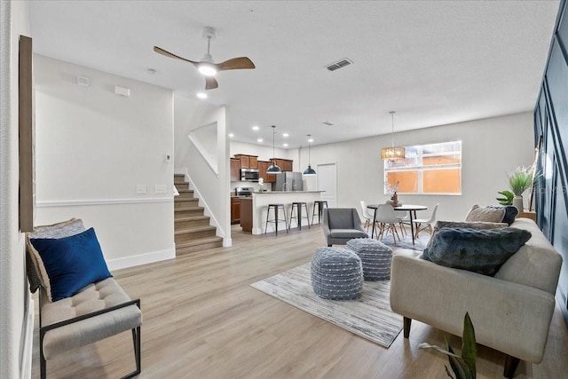 living room featuring a textured ceiling, ceiling fan with notable chandelier, and light hardwood / wood-style flooring