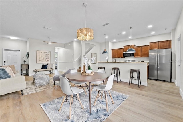 dining space with light hardwood / wood-style floors and ceiling fan with notable chandelier