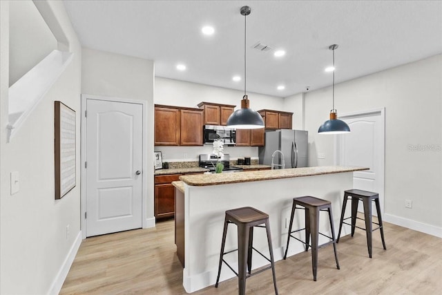 kitchen featuring a center island with sink, a kitchen breakfast bar, hanging light fixtures, light hardwood / wood-style flooring, and appliances with stainless steel finishes