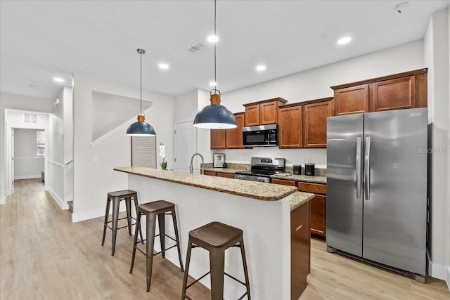 kitchen featuring decorative light fixtures, stainless steel appliances, a kitchen breakfast bar, and an island with sink