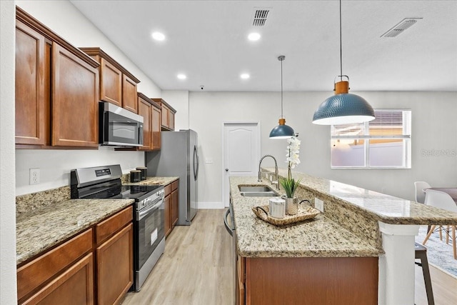 kitchen with sink, hanging light fixtures, light wood-type flooring, an island with sink, and stainless steel appliances