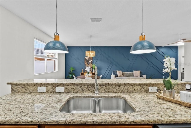 kitchen with light stone counters, sink, and decorative light fixtures