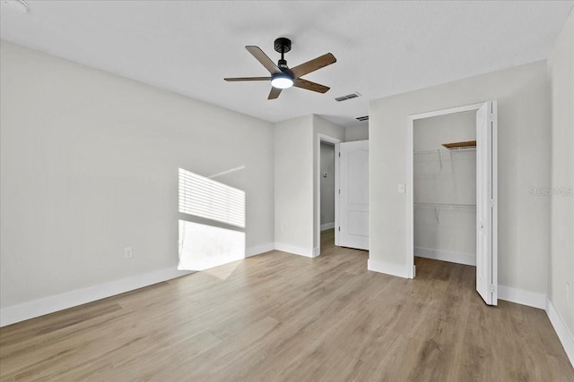 unfurnished bedroom with a spacious closet, ceiling fan, light wood-type flooring, and a closet