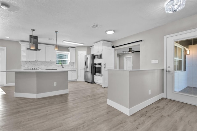 kitchen featuring white cabinets, pendant lighting, light wood-type flooring, and stainless steel appliances