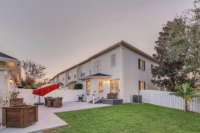 back house at dusk featuring a yard, cooling unit, and a patio