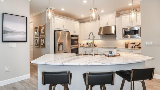 kitchen with a large island with sink, decorative light fixtures, light stone counters, white cabinetry, and stainless steel appliances