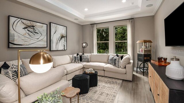 living room with wood-type flooring, a tray ceiling, and crown molding