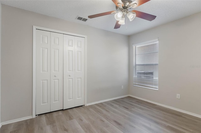 unfurnished bedroom with a textured ceiling, light wood-type flooring, a closet, and ceiling fan