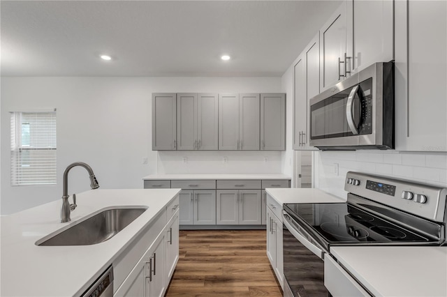 kitchen with sink, dark wood-type flooring, gray cabinets, decorative backsplash, and appliances with stainless steel finishes