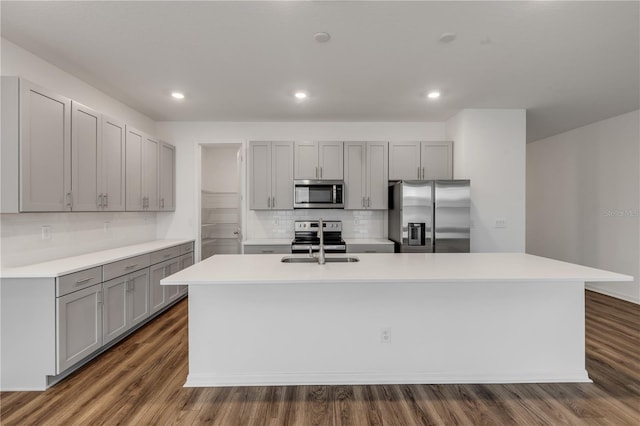 kitchen featuring appliances with stainless steel finishes, dark hardwood / wood-style flooring, a center island with sink, and tasteful backsplash