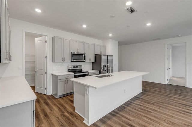 kitchen with sink, dark hardwood / wood-style flooring, gray cabinets, a kitchen island with sink, and appliances with stainless steel finishes