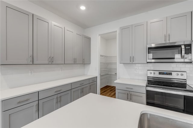 kitchen with decorative backsplash, appliances with stainless steel finishes, gray cabinets, and dark wood-type flooring