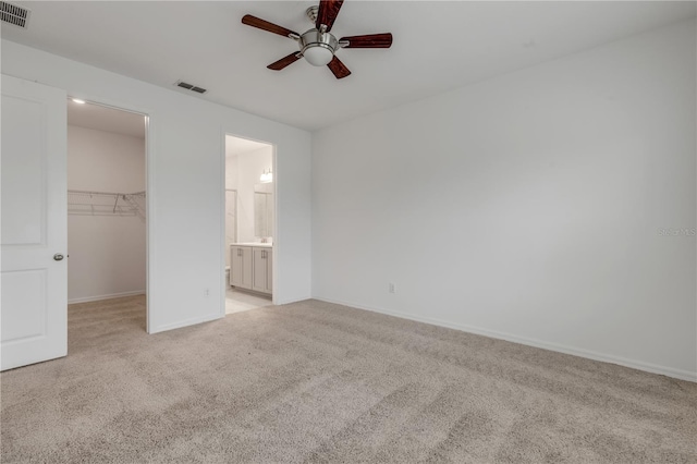 unfurnished bedroom with ensuite bath, ceiling fan, a walk in closet, light carpet, and a closet