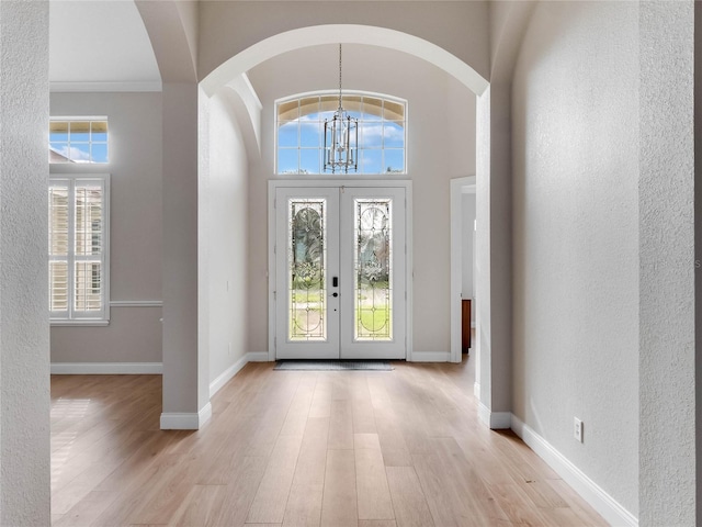 entryway with a chandelier, light wood-type flooring, ornamental molding, and french doors